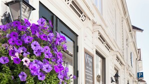 A building with a large planter of purple flowers in front of the entrance. - Kjøbmandsgaarden Hotel (Lindesnes)
