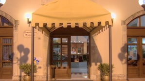 La entrada del Hotel Fortezza, con un porche cubierto, suelo de baldosas y dos macetas.