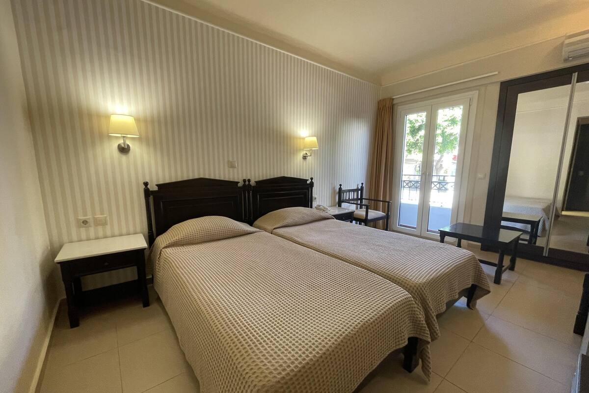 Habitación de hotel con dos camas, un escritorio y una silla. Hay dos lámparas fijadas a la pared.