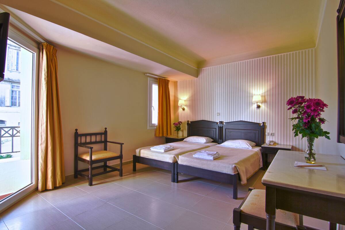 Habitación de hotel con dos camas, una silla, una mesa y un ventanal con cortinas.