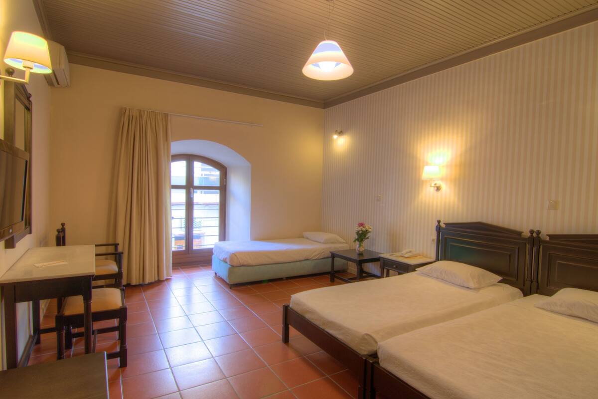 Habitación de hotel con dos camas, un escritorio, sillas, una mesita y una ventana con cortinas.