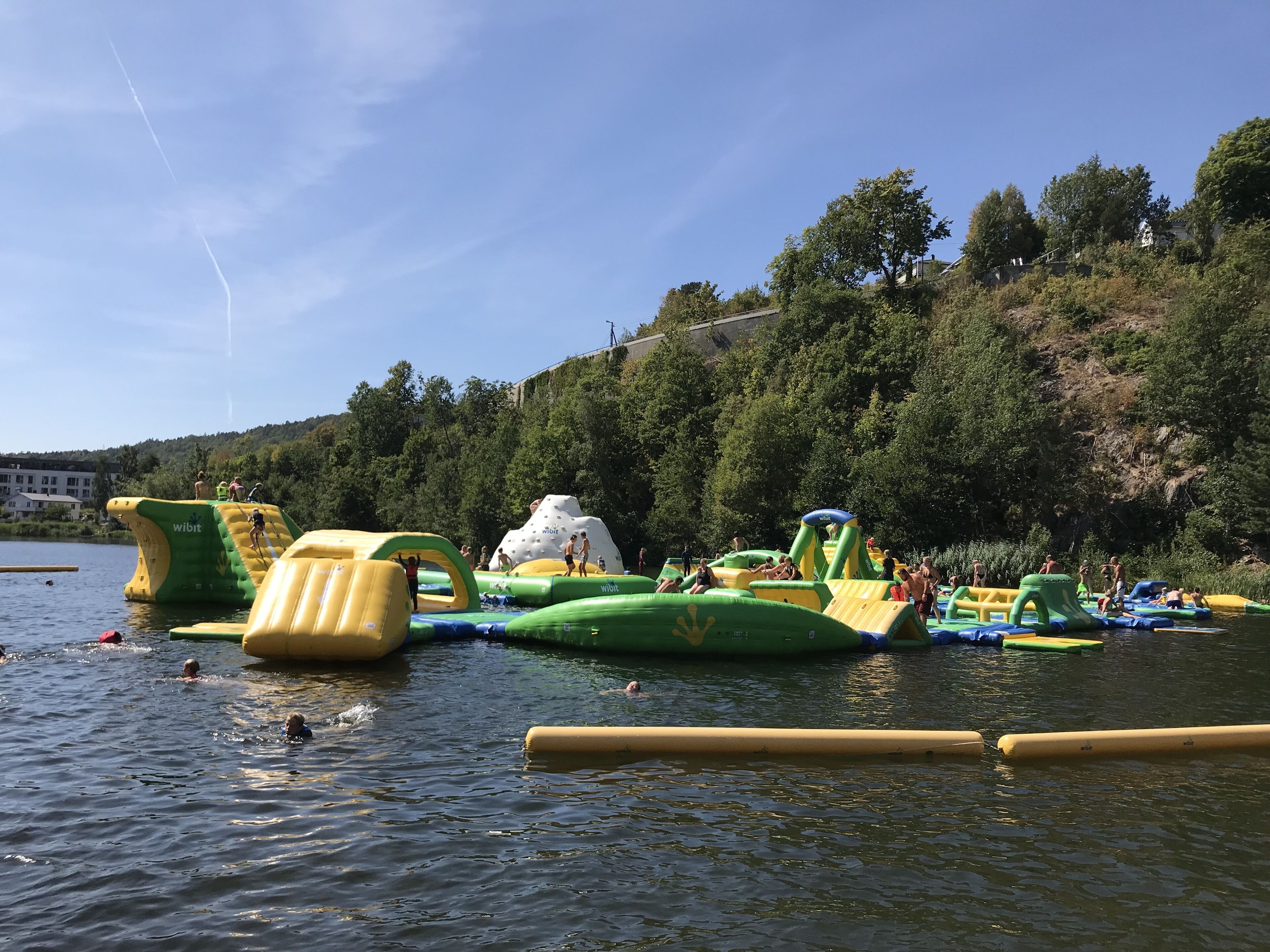 Parque acuático al aire libre con estructuras inflables y un lago.