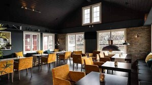 Un ristorante con soffitti alti, travi in legno e ampie finestre. Tavoli e sedie disposti per la ristorazione.