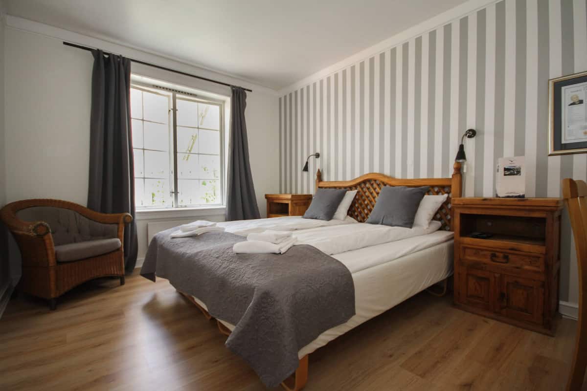 A neatly arranged bedroom with a large bed, two bedside tables, a wooden chair, and a window with curtains.