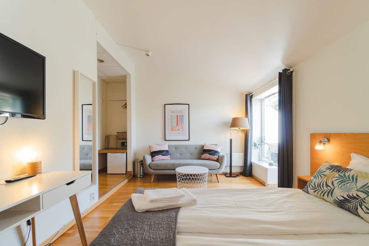 A modern hotel room with a large bed, a desk, a sofa, and a TV.