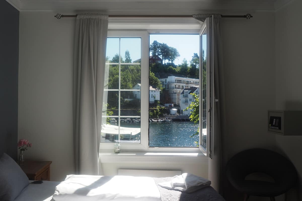 A hotel room with a large window offering a view of a body of water and buildings.