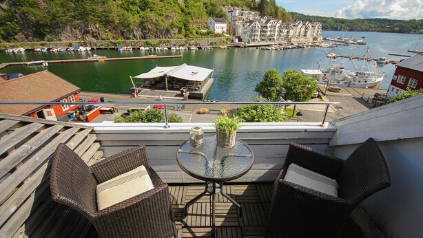 Un balcone con mobili in vimini, un tavolo in vetro e vista su un porto con barche ed edifici.