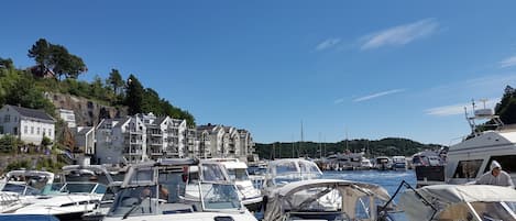 A marina with multiple boats docked, a building with balconies, and a clear blue sky.
