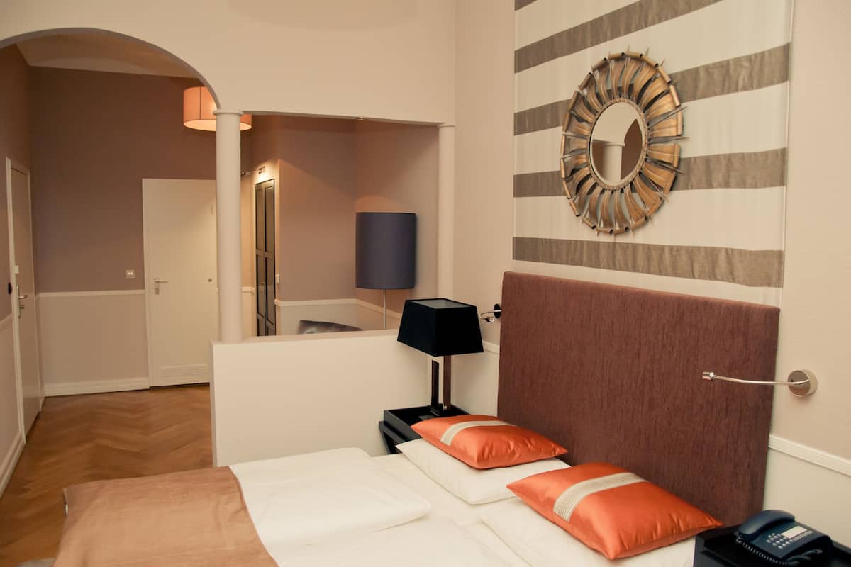 A hotel room with a bed, a nightstand, a lamp, a mirror, and a striped wall.