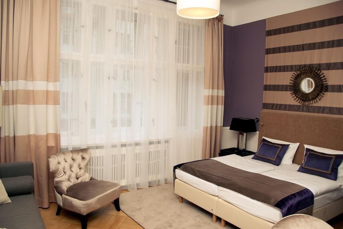 A bedroom with a bed, a chair, a nightstand, and a wall-mounted mirror.