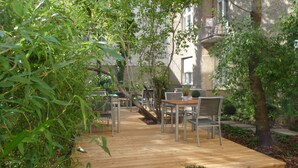 An outdoor patio area with wooden flooring, metal tables and chairs, and potted plants. - Hotel Elba am Kurfürstendamm - Design Chambers (Berlin)