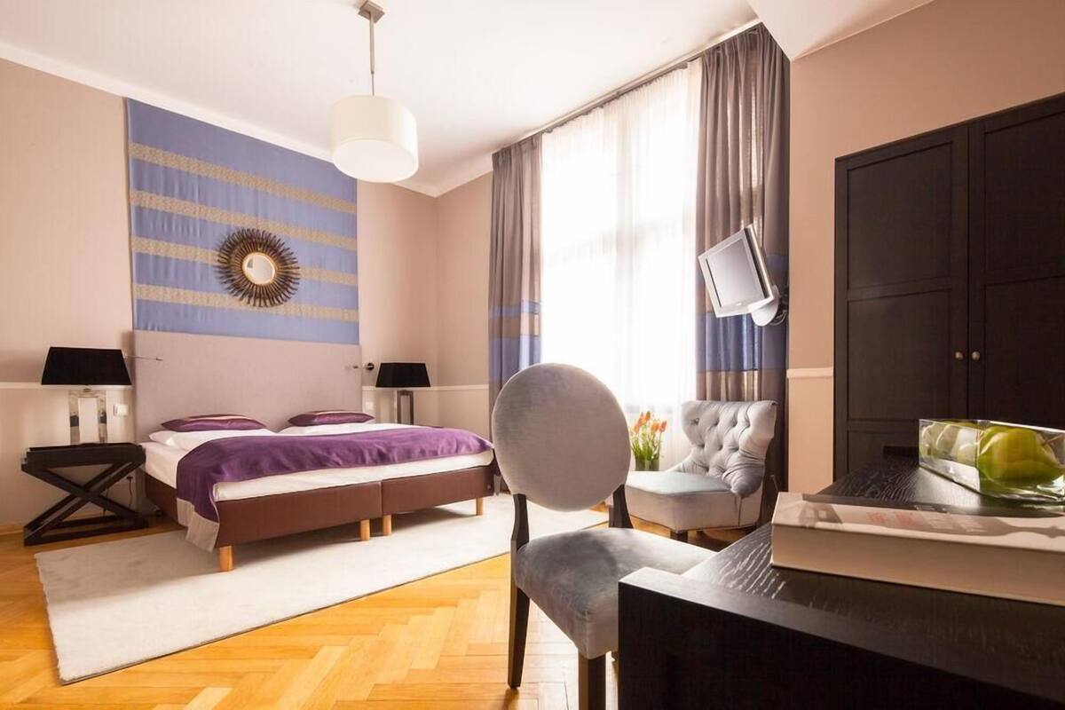 A hotel room with a bed, a desk, a chair, a TV, and a large window with curtains.