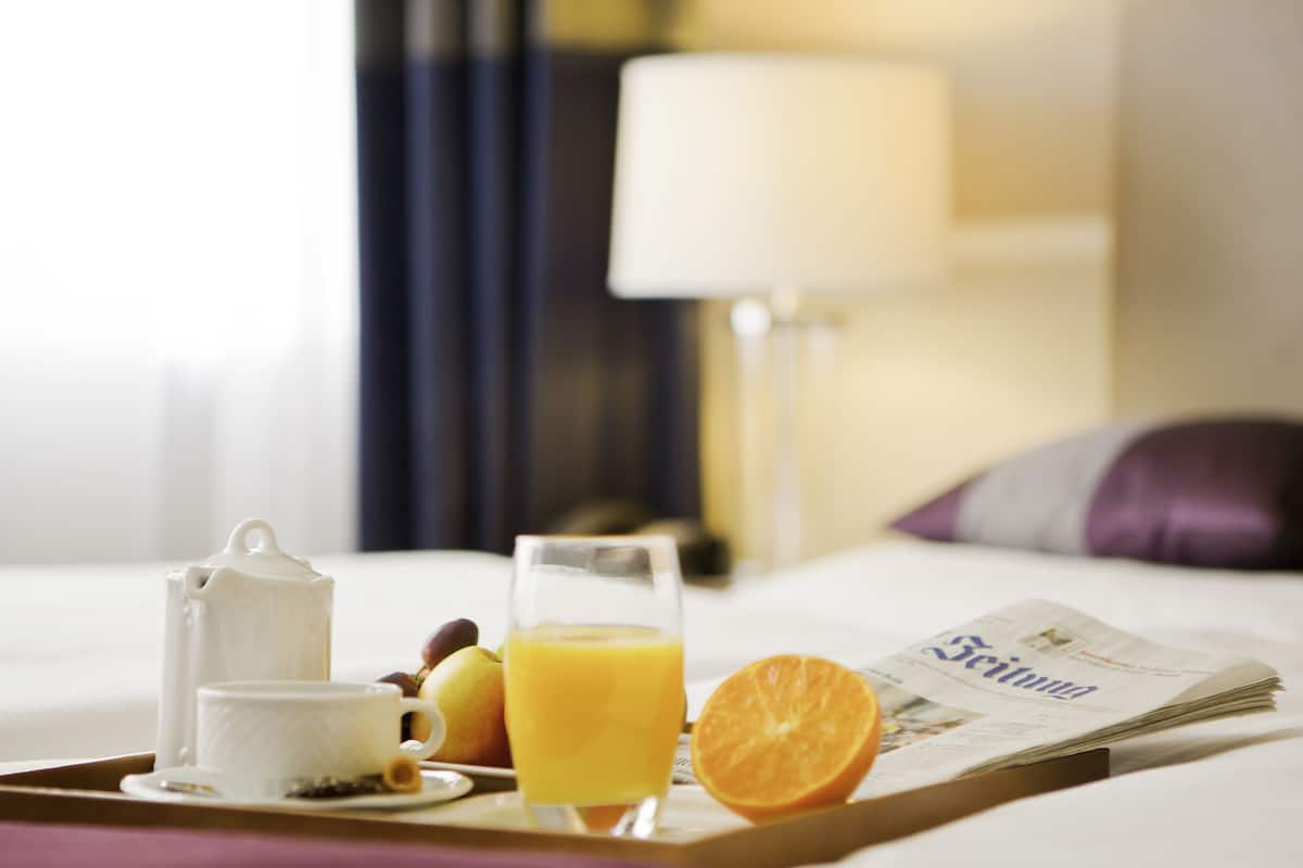 A breakfast tray with a teapot, cup, orange juice, and fruit on a hotel bed.