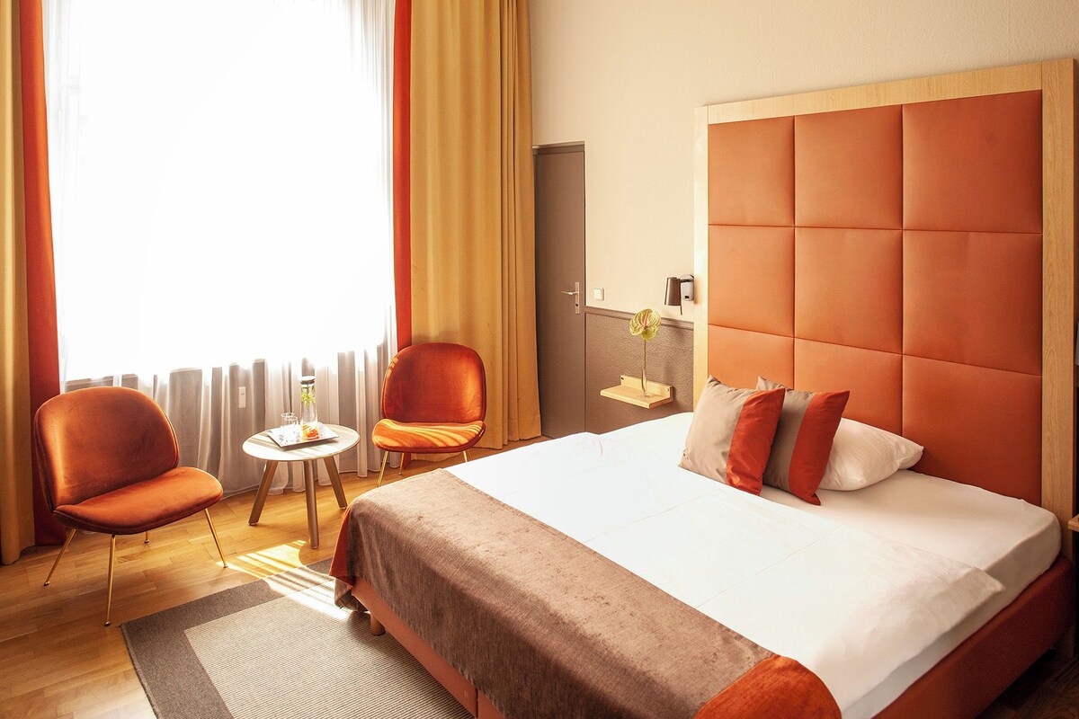 A hotel room with a large bed, two chairs, a small table, and a nightstand.