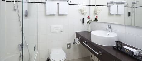 Un baño moderno con cabina de ducha de vidrio, un inodoro blanco y un mueble de tocador oscuro con lavabo y toallero.