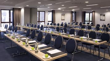 Un salón de conferencias con mesas largas, sillas, botellas de agua y manzanas.