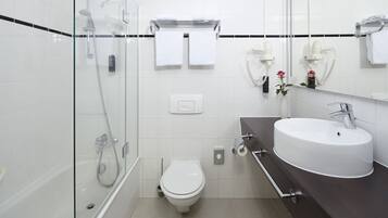 A modern bathroom with a glass-enclosed shower, a white toilet, and a dark-colored sink with a mirror above it.