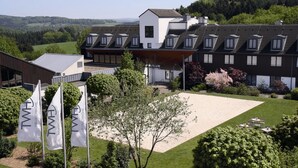 Un hotel moderno con varios pisos, un área exterior cubierta y banderas que identifican una ubicación Kränichhof.
