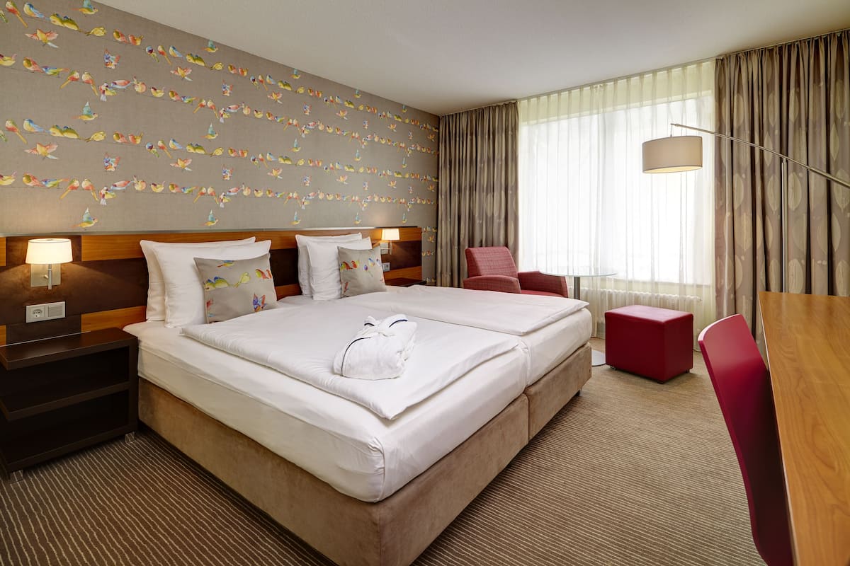 A hotel room with a large bed, a desk, a chair, and a window with curtains.