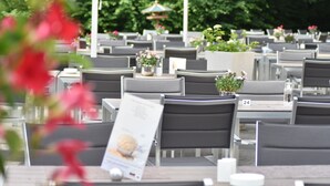 Mesas de comedor al aire libre con sillas, algunas con plantas en macetas y un atril para el menú.