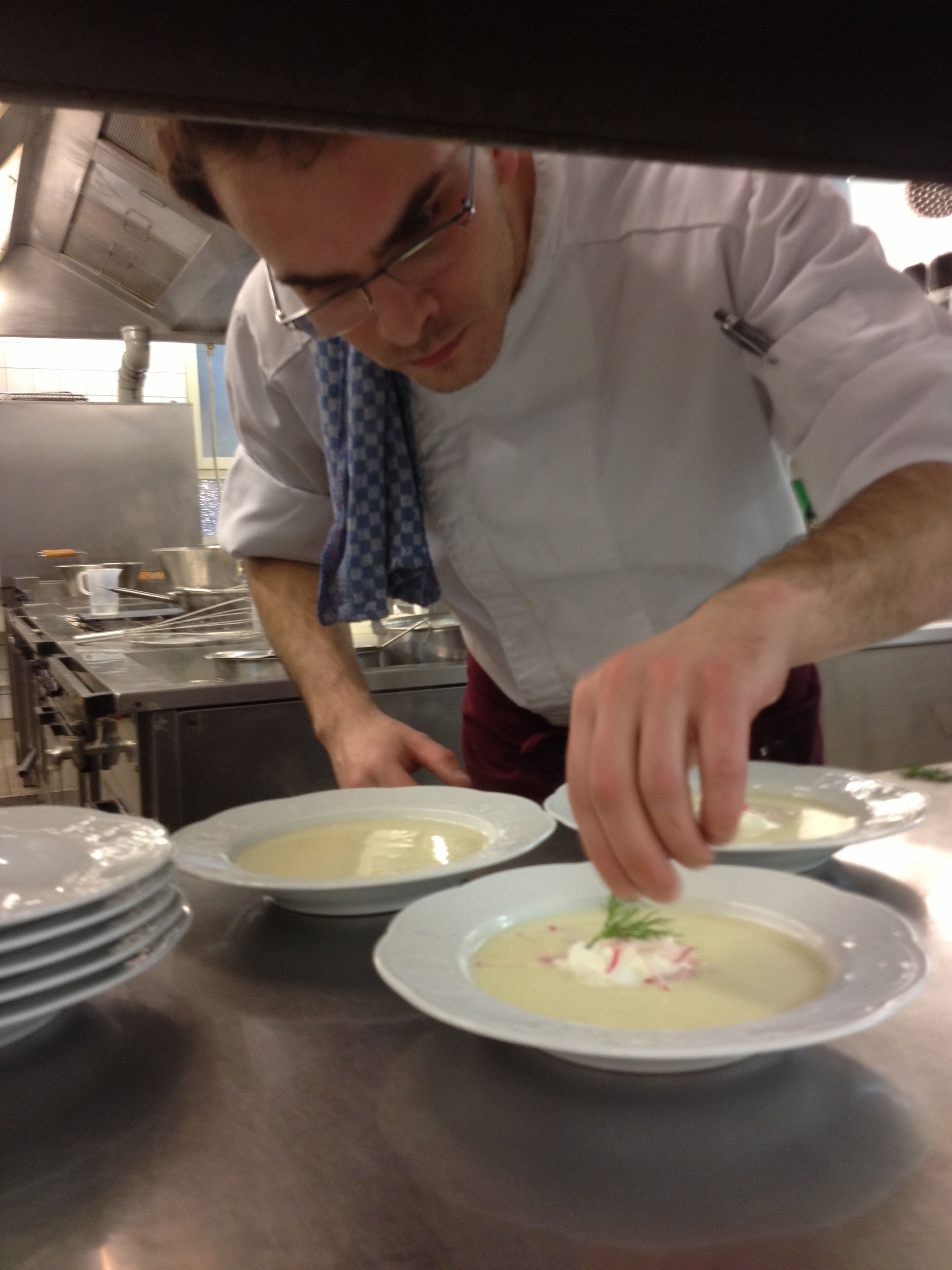A chef preparing dishes in a professional kitchen with stainless steel equipment and multiple plates of food.