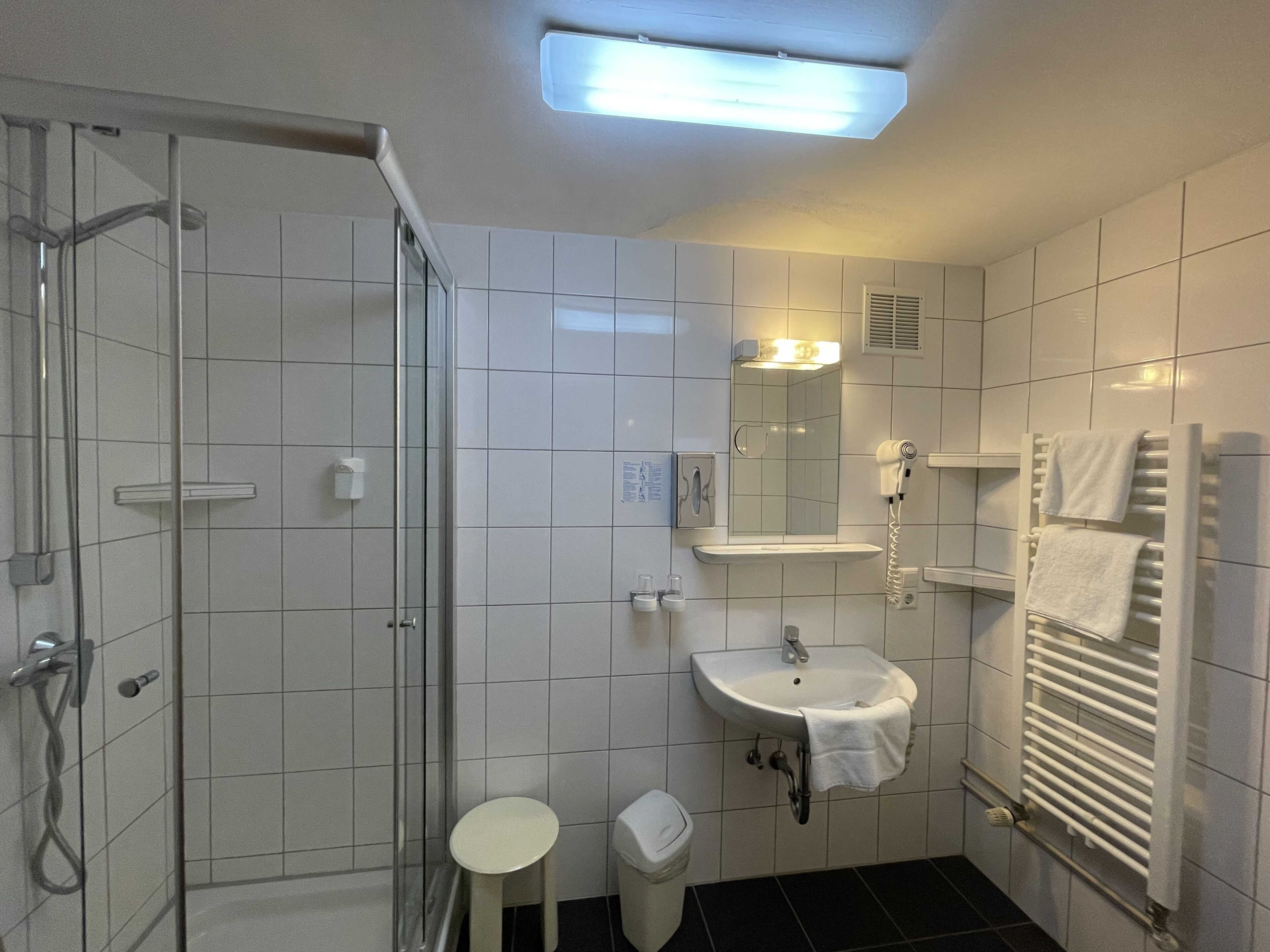 Un baño moderno con cabina de ducha de vidrio, un lavamanos y una toalla colgada en la pared, y un radiador blanco.