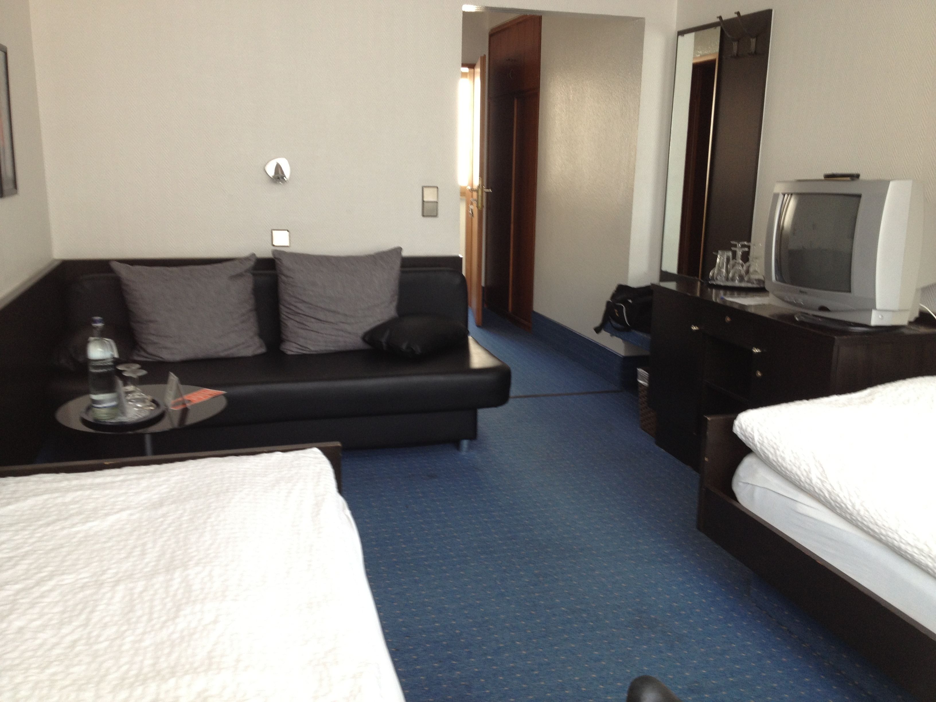 Una habitación de hotel con cama, sofá, televisión y escritorio con lámpara.