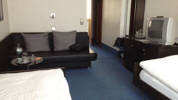 Una habitación de hotel con cama, sofá, televisión y escritorio con lámpara.