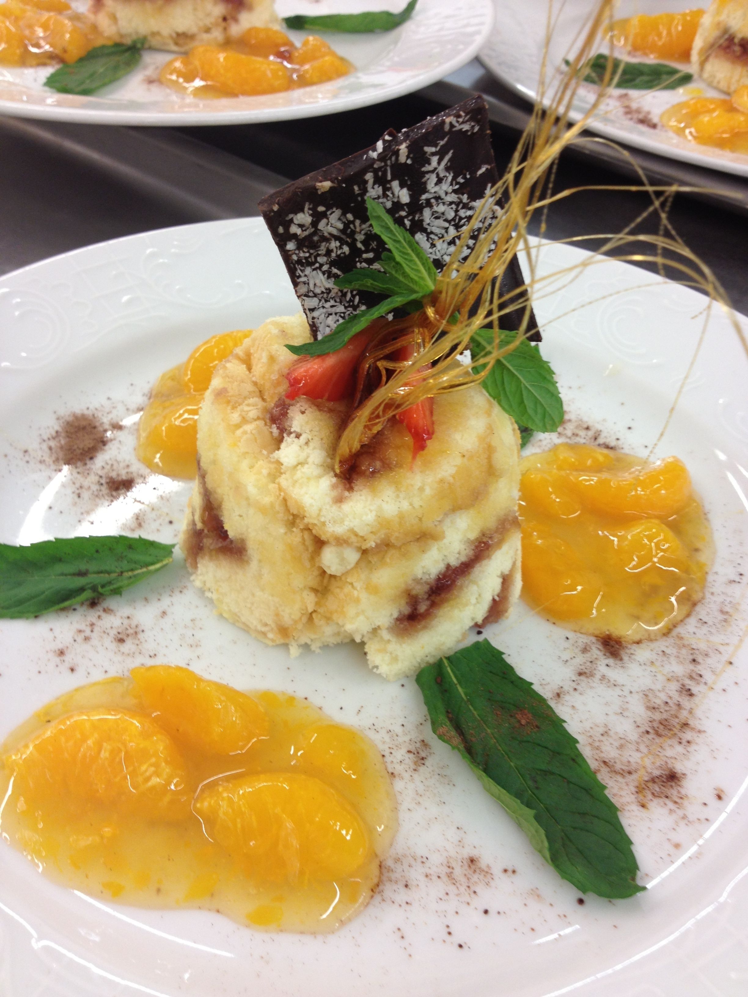 Une assiette de dessert avec un gâteau à plusieurs couches, des segments d’orange et des feuilles de menthe.