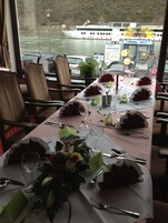 Mesa lista para una comida, con vistas a un río y un barco al fondo.