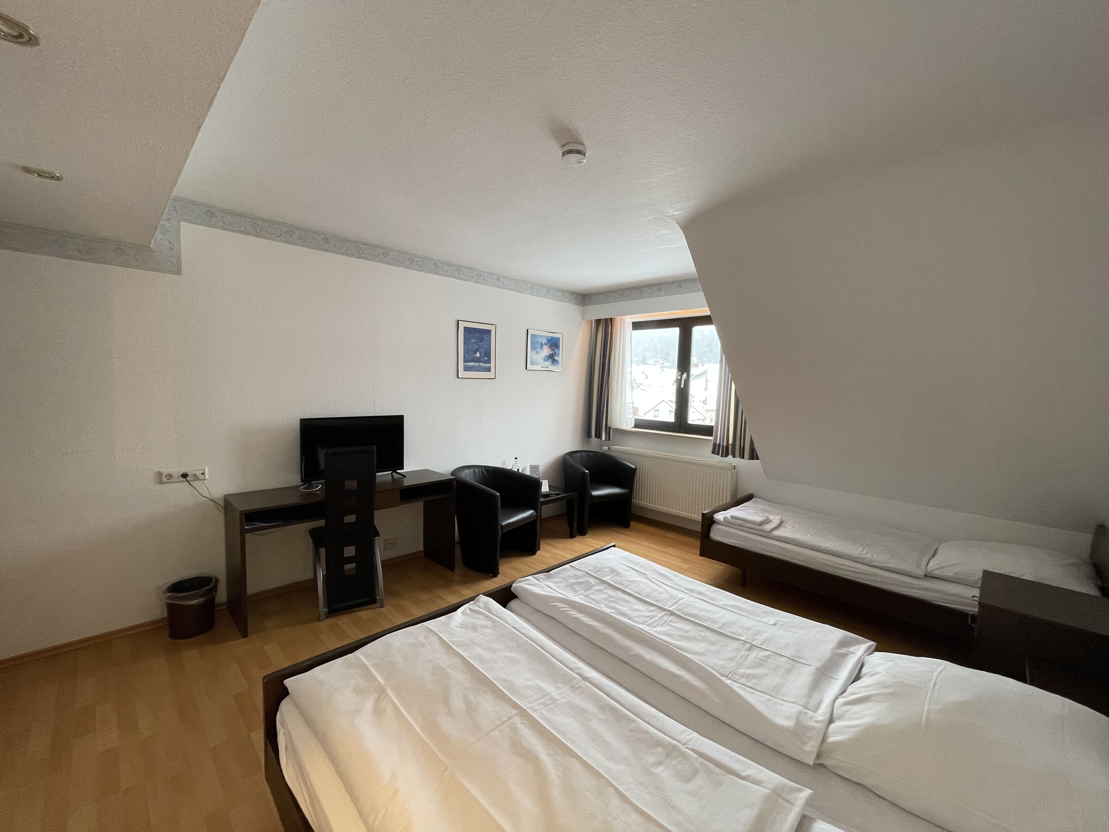 A room with two beds, a desk with a chair, a television, and a window with curtains.