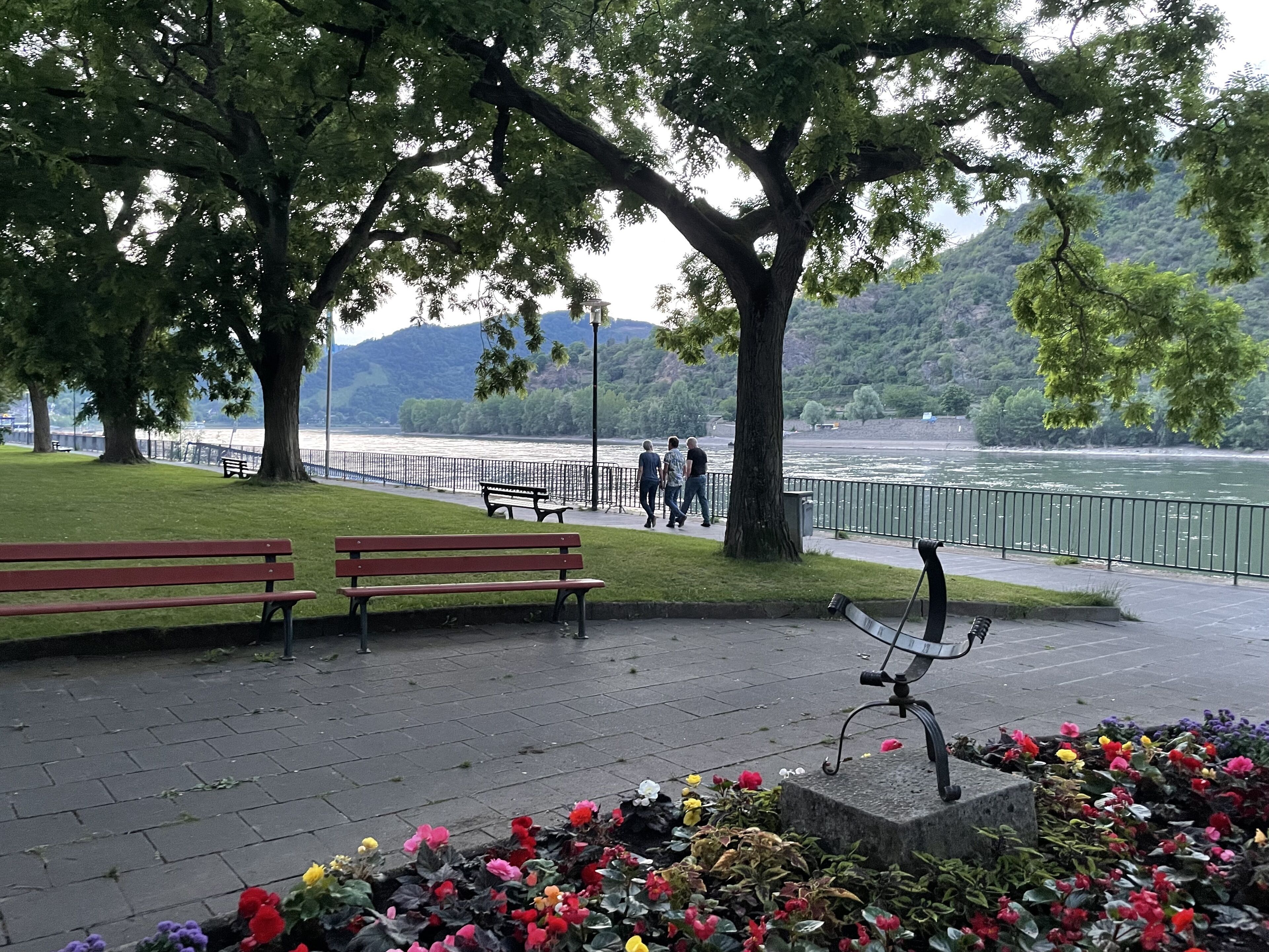A riverside park with benches, a walking path, and flower beds.