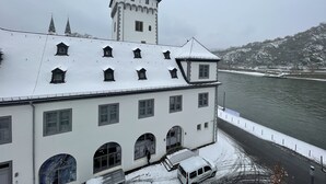 A historic building with a tower, arched windows, and a river in the background. - Hotel Rheinlust (Boppard)