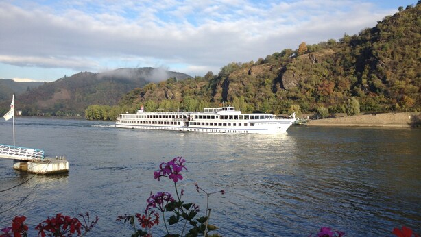A large river cruise ship named "Staten Island" on a calm river with a dock in the foreground and a forested hillside in the background. - Hotel Rheinlust (Boppard)