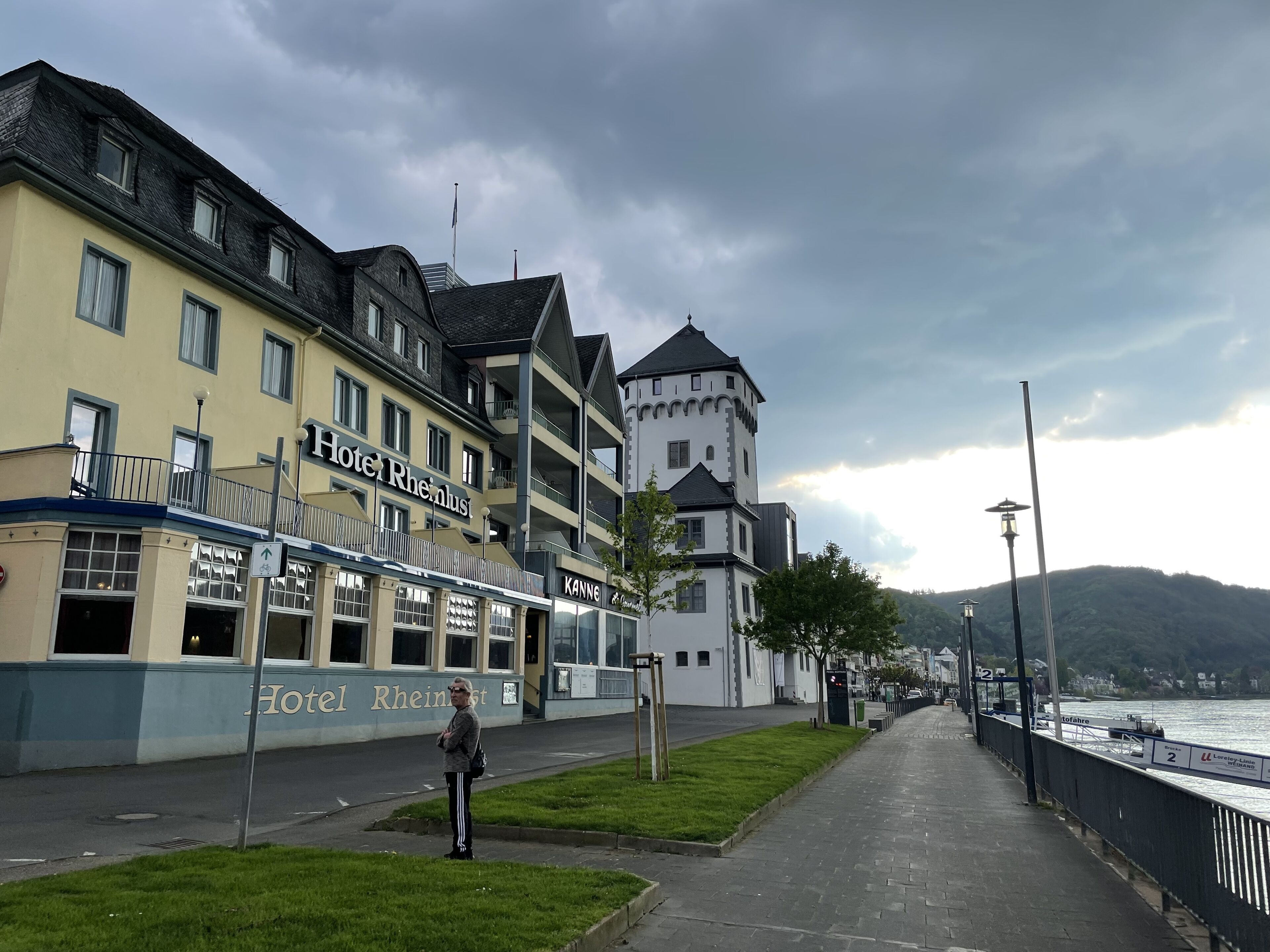 A hotel with a tower and a sign for 'Hotel Rheinlust' along a waterfront promenade.