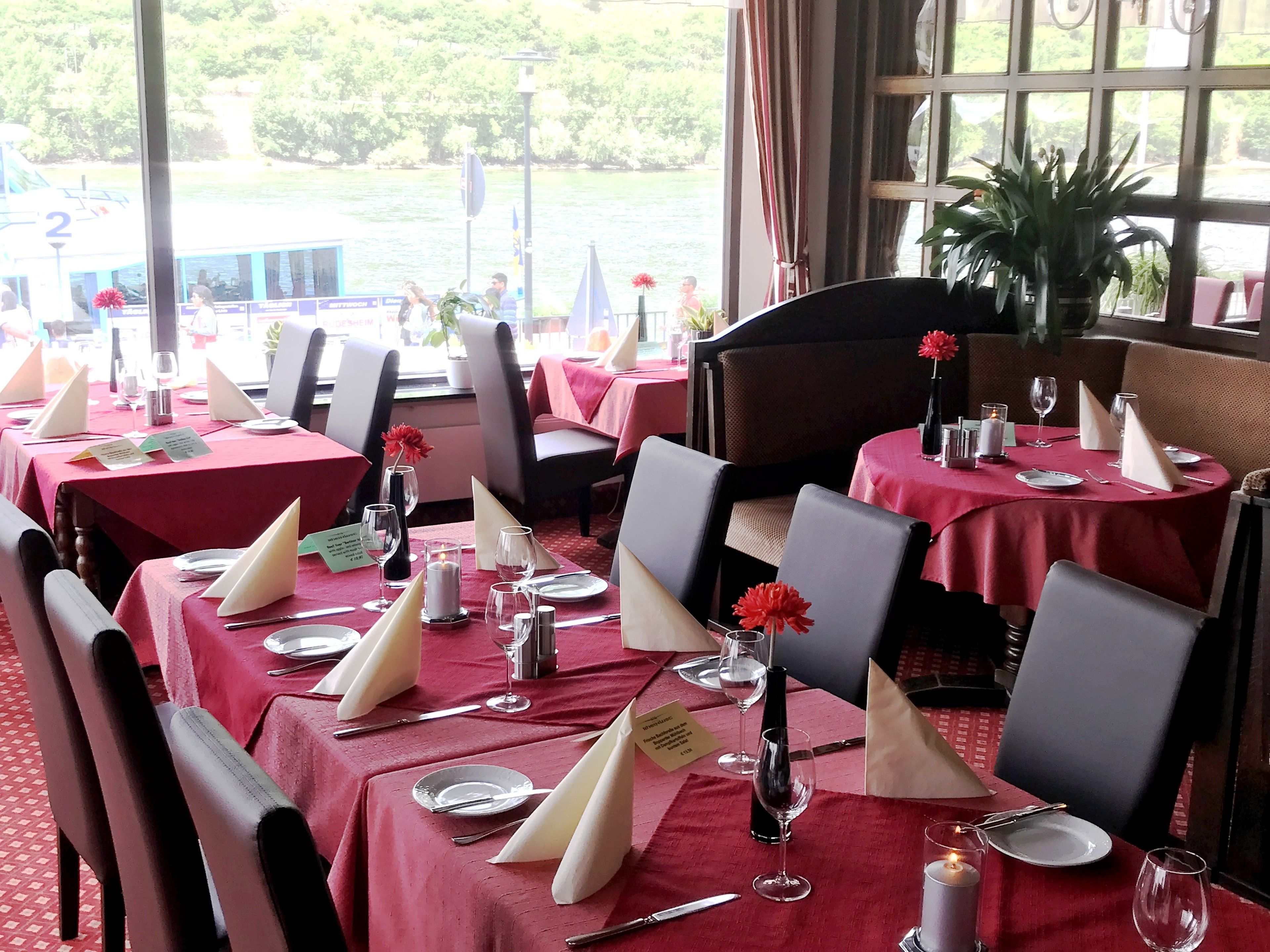 A restaurant with tables set for dining, featuring red tablecloths and white napkins.