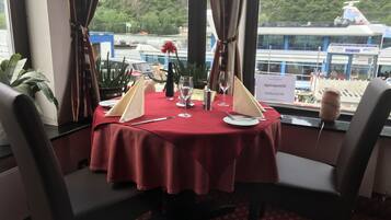 Una mesa de comedor con mantel rojo, dos sillas, un menú, una copa de vino y una vela.