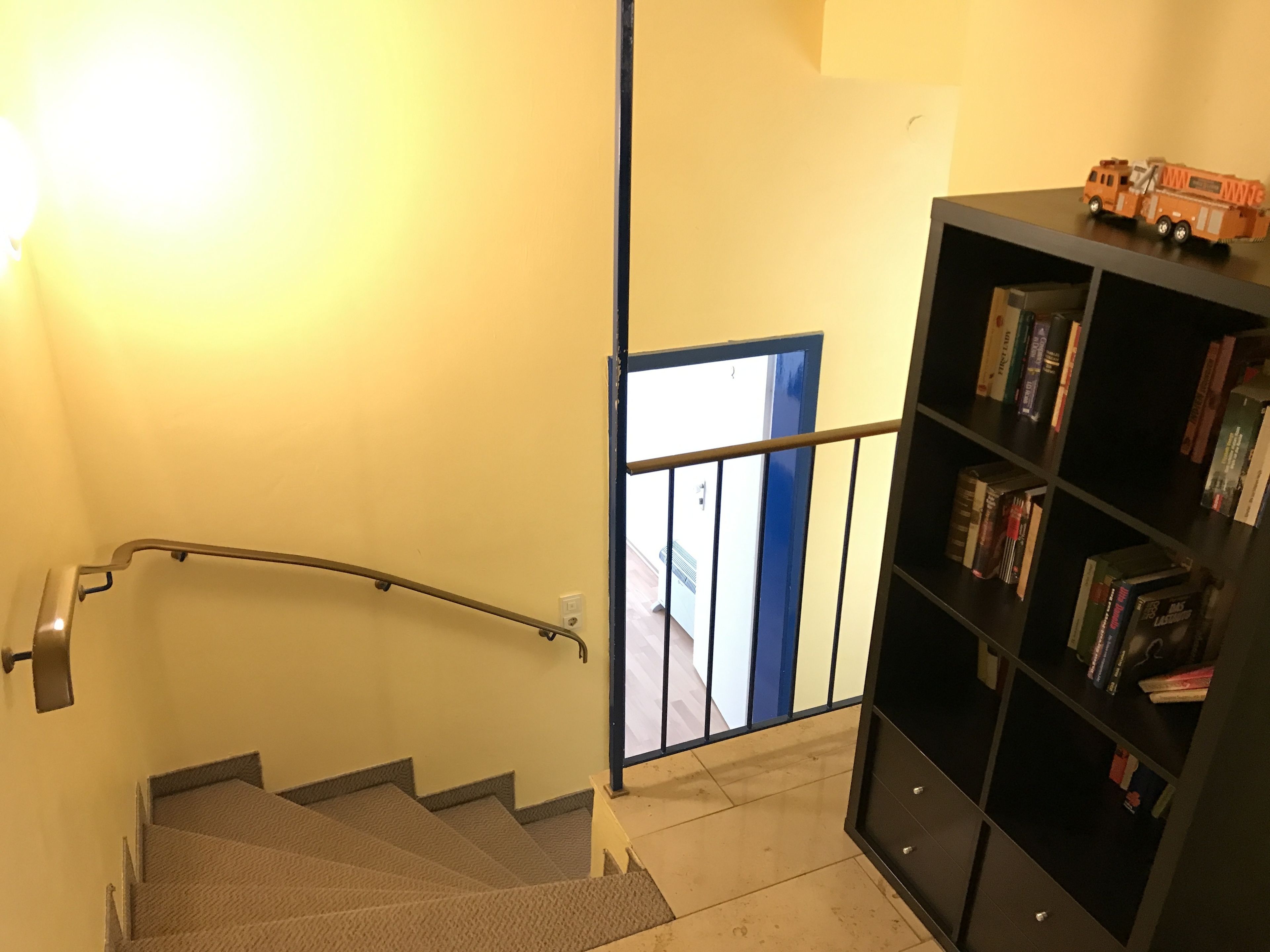 Un escalier avec une rampe menant à un palier, une bibliothèque remplie de livres et une porte donnant sur un espace extérieur.