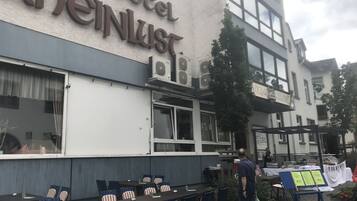 A hotel exterior with outdoor seating, a sign reading "hotel Rheinlust," and a person standing near the entrance.