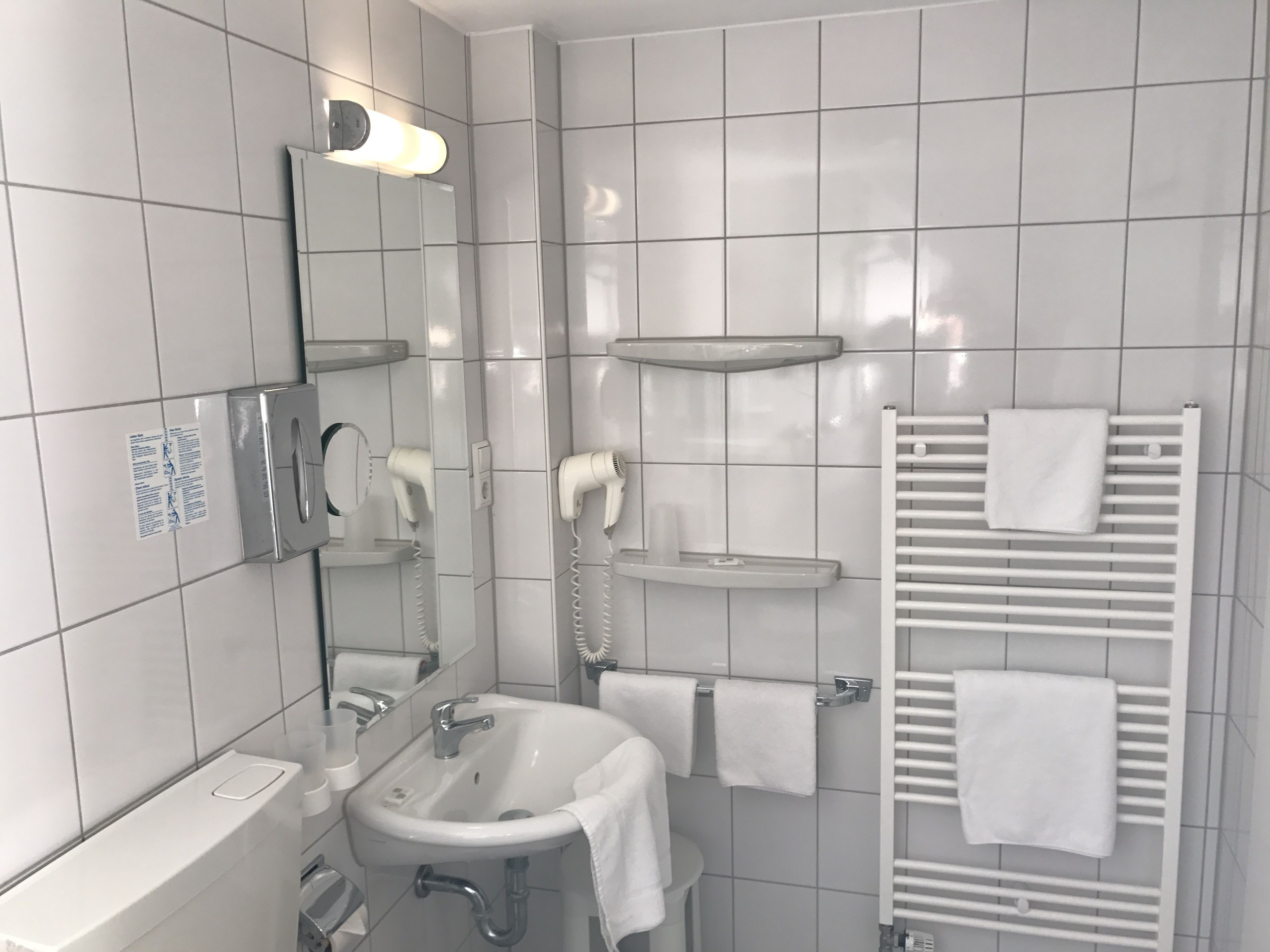 A modern bathroom with a sink, mirror, hair dryers, and a towel rack.