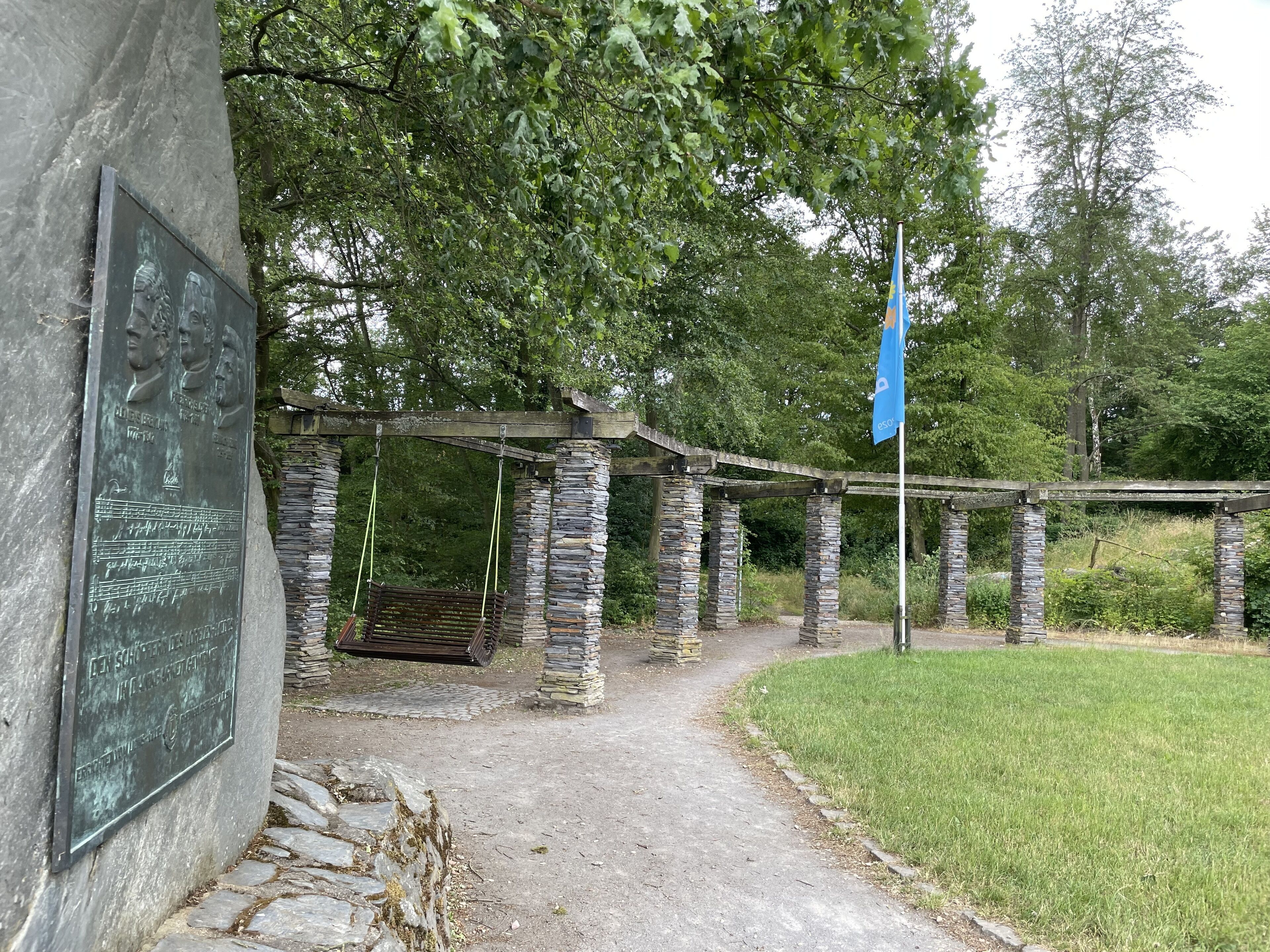 A stone structure with a swing, a plaque, and a flag.