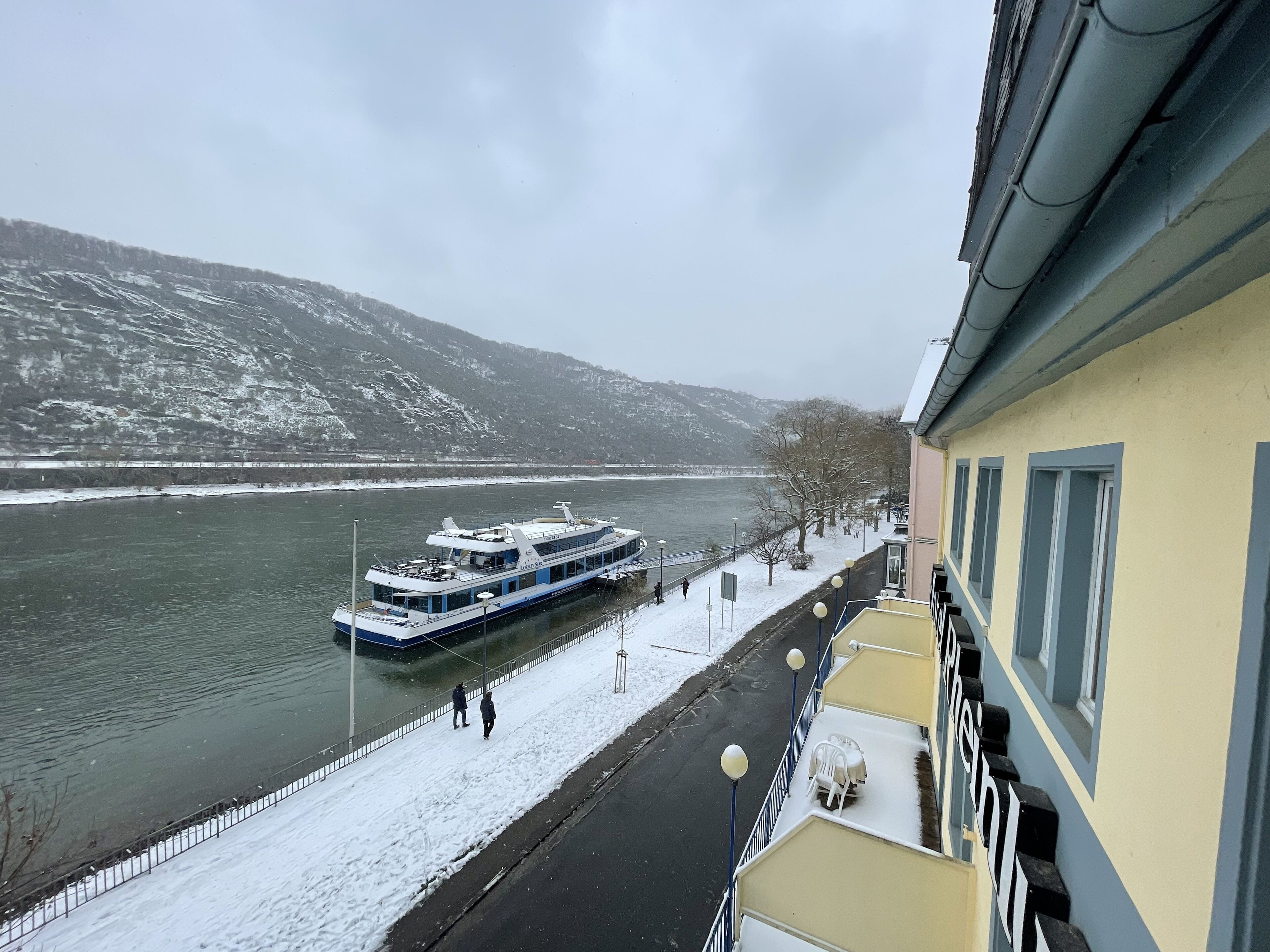 Ein Fluss mit einem Boot, verschneiter Boden und ein Gebäude mit einem Balkon.