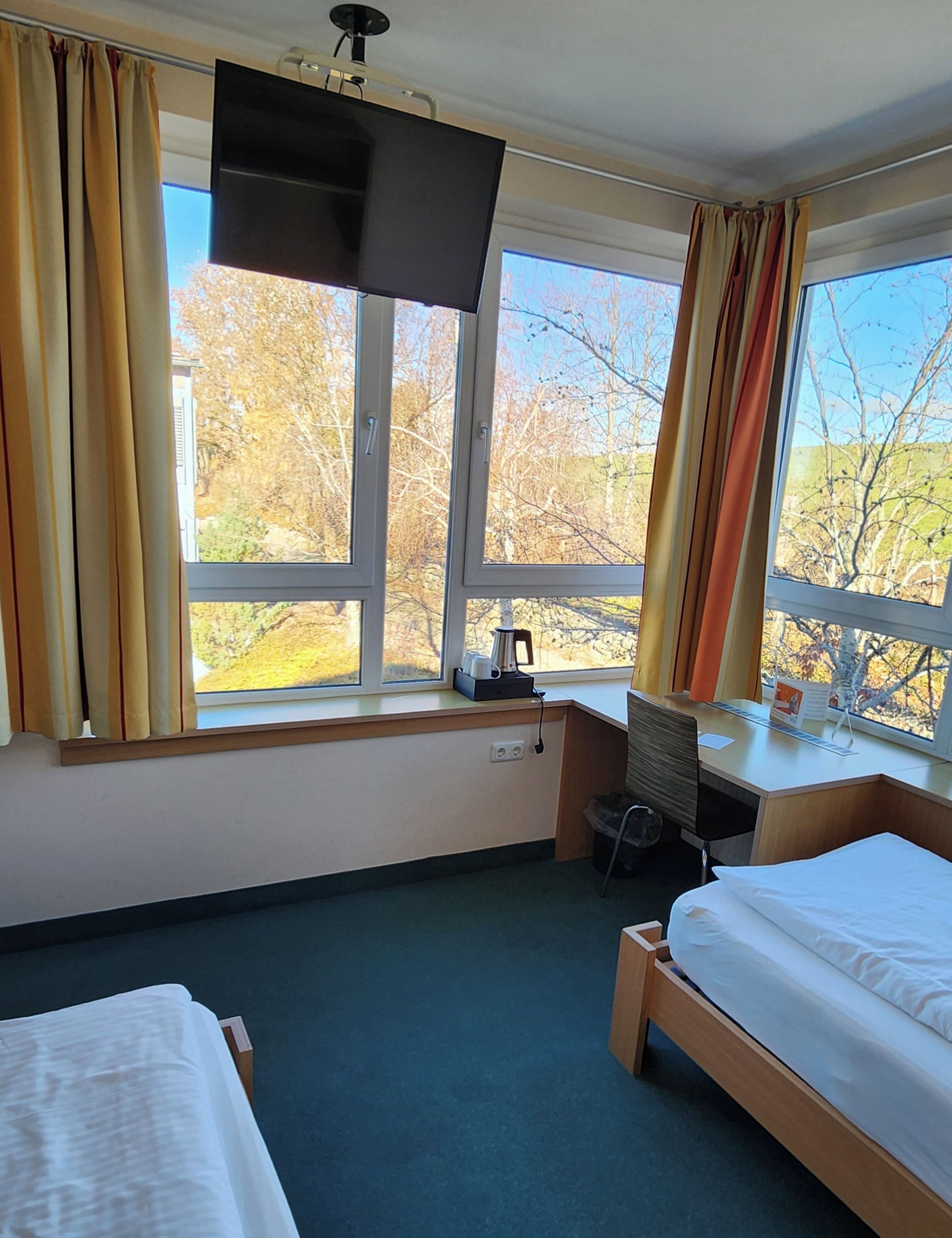 A hotel room with two beds, a desk, a chair, and a TV.
