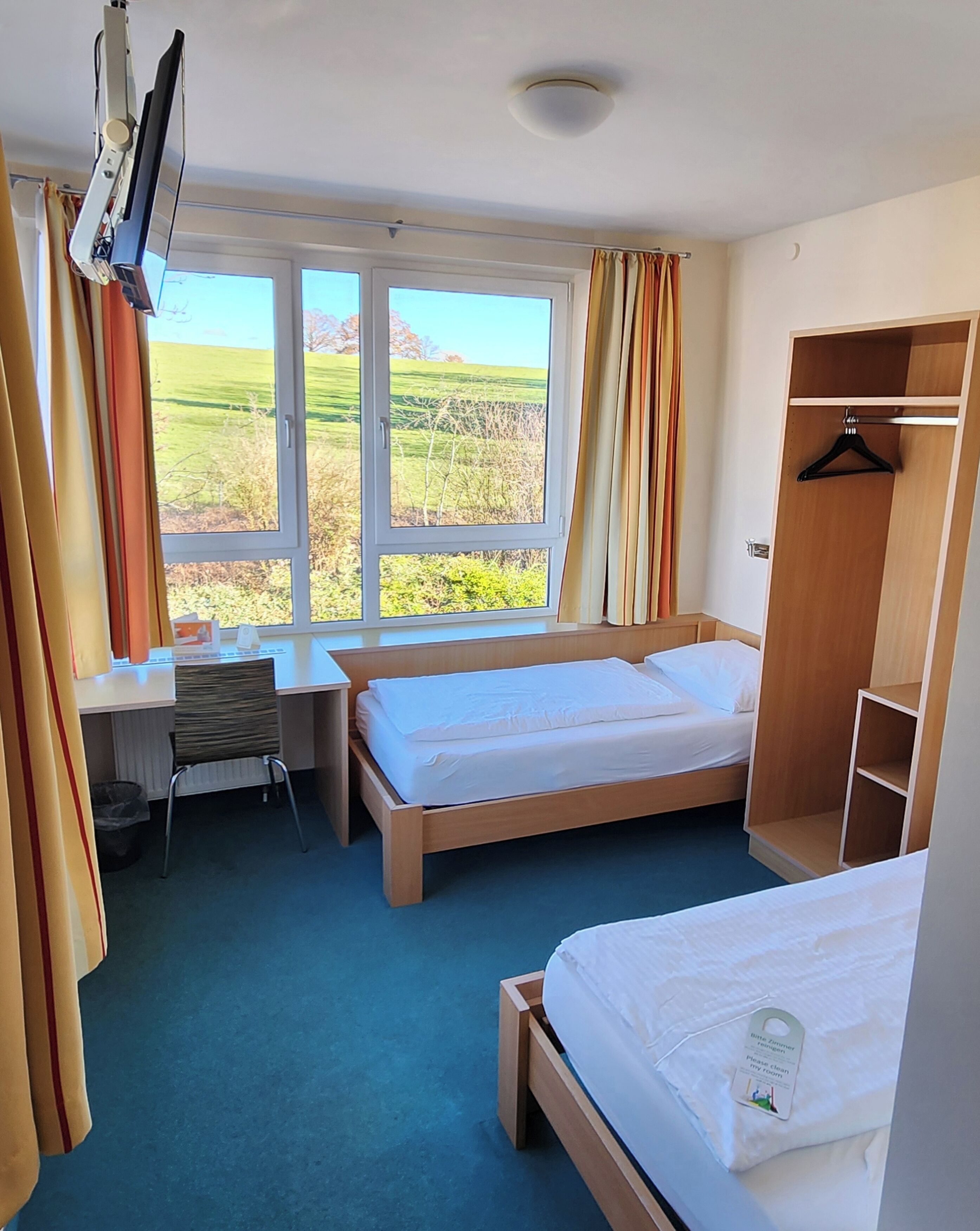 Habitación de hotel con dos camas, un escritorio, una silla, un televisor y un armario.