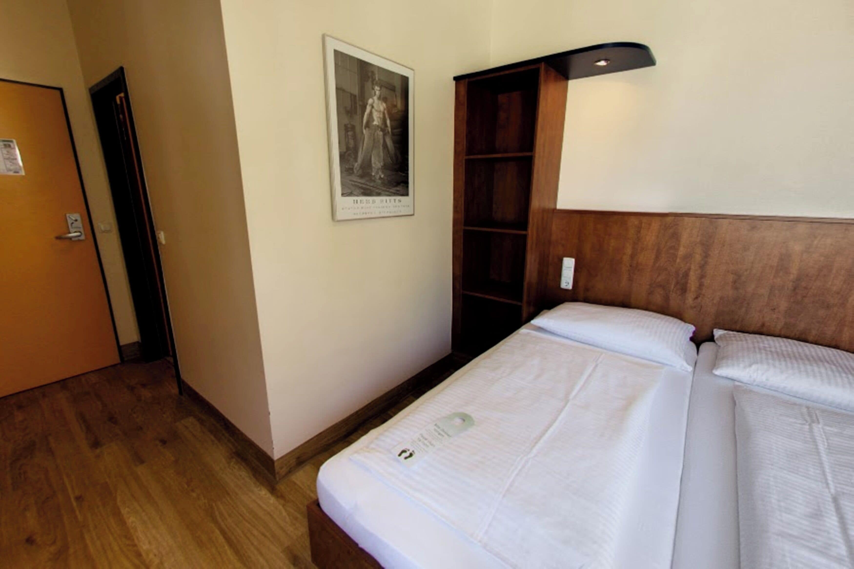 A hotel room with a wooden headboard, a poster on the wall, and a door to the left.