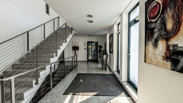 Un interior moderno con una escalera, un cuadro abstracto grande y una puerta que da a otra habitación.