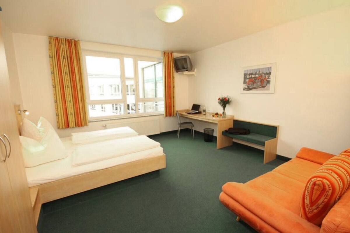 A hotel room with two beds, a desk, a chair, a TV, and a window with curtains.