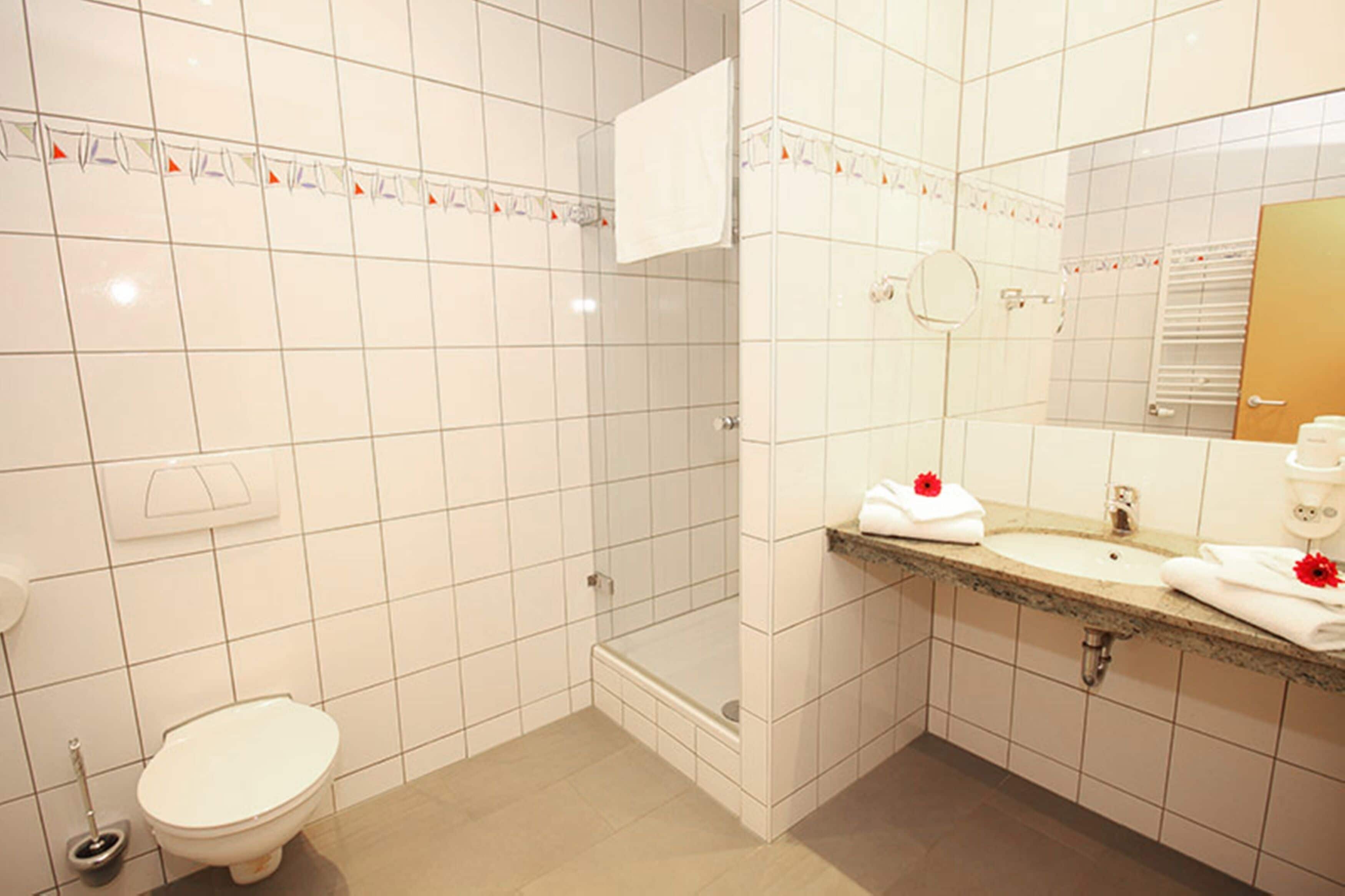 A bathroom with a toilet, shower, sink, and mirror.