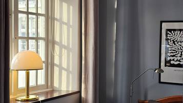 Un dormitorio con cama, lámpara de noche, radiador, ventana con cortinas y aplique de pared.