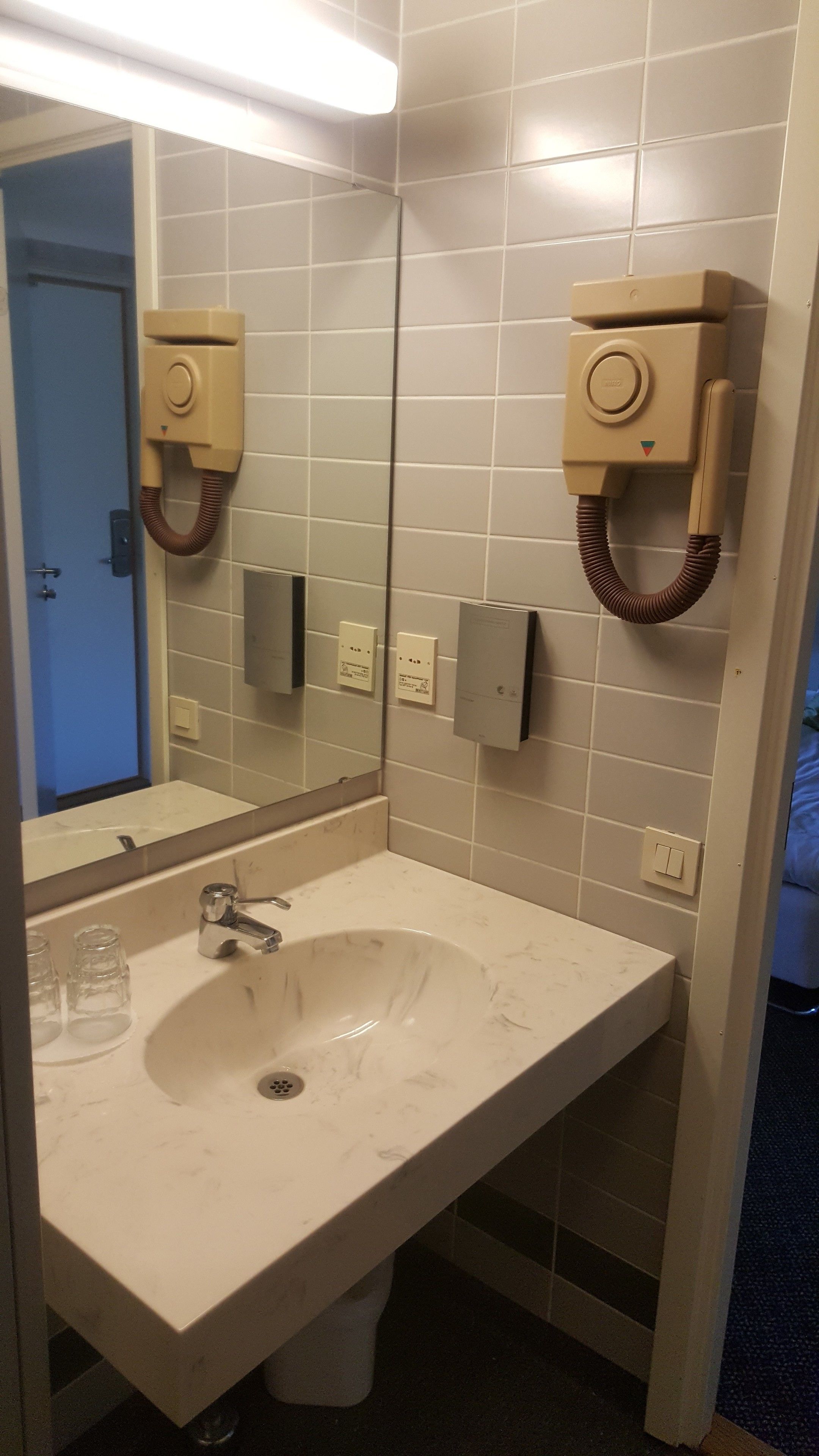 A bathroom with a white sink, mirror, and two towel dispensers.